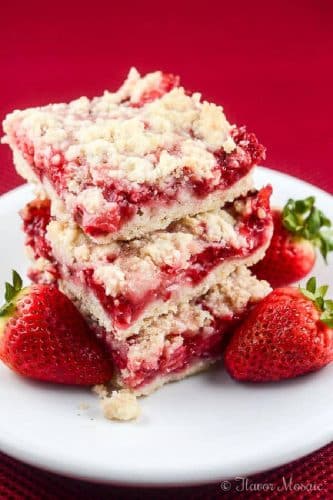 3 Strawberry Crumb Bars on a white plate surrounded by fresh strawberries with a bright pink background.