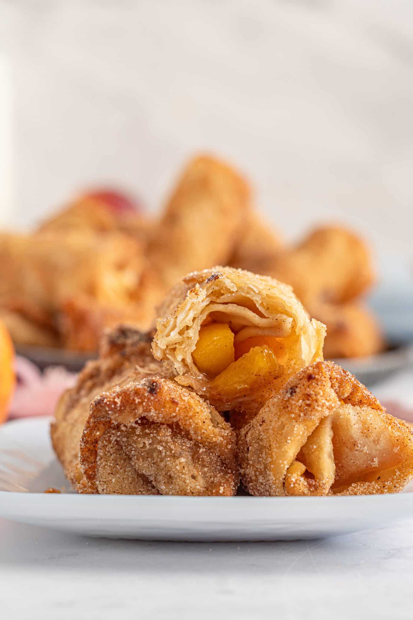 Side view of peach cobbler egg rolls with one egg roll cut in half so you can see the peaches inside the egg roll.