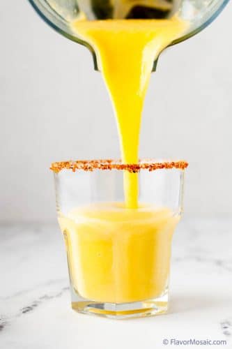 Pouring a mango jalapeno margarita into a glass.