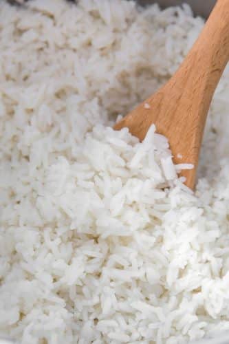 Close up of cooked white rice in a pan with a wooden spoon.
