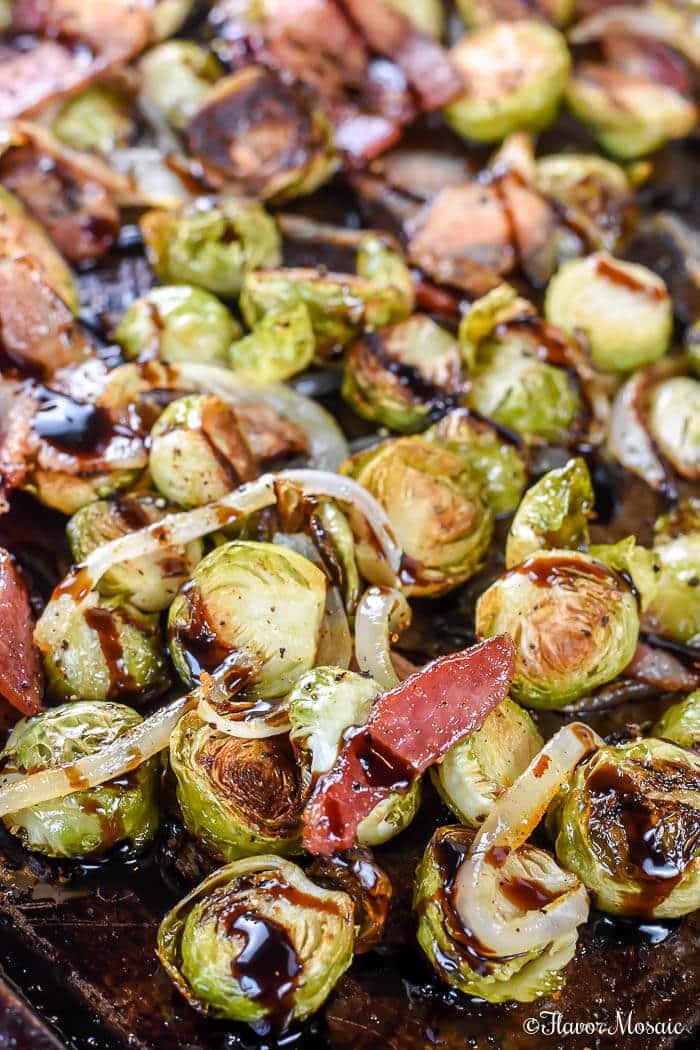 Roasted Brussels sprouts with crispy bacon and drizzled in balsamic vinegar on a baking sheet.