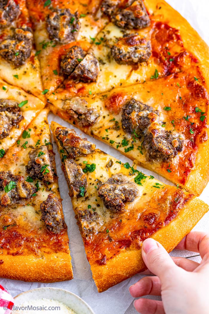 Close up of pizza after it has been cooked and sliced, and someone is starting to pull one slice of pizza away from the rest of the meatball pizza.