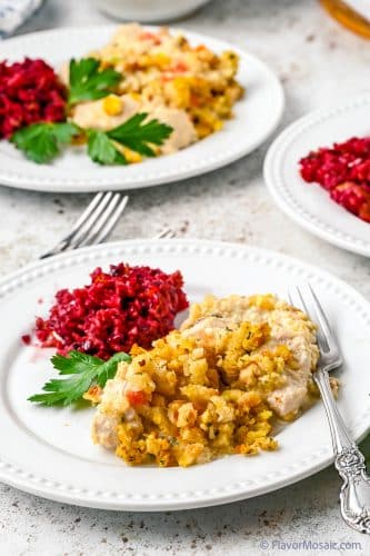 a white plate with chicken and stuffing casserole, parsley and cranberry plate, and another identical plate in the back and a partial view of a 3rd plate on the right but can only see part of the cranberry sauce.