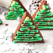 Christmas Tree Brownies with green icing standing vertically with a white background a "snow-covered" pinecone in the background.