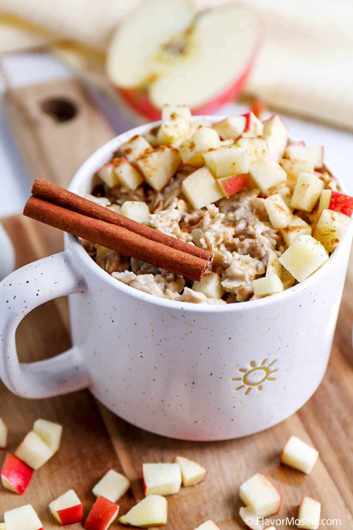 Close up of Apple Oatmeal Custard in a mug topped with a chopped red apple and garnished with 2 cinnamon sticks.