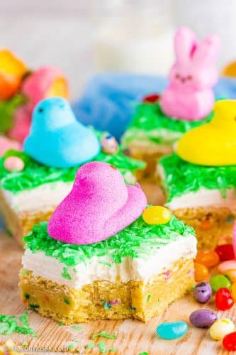 Side view of multiple Easter Sugar Cookie Bars topped with cream cheese, green coconut "grass", jelly beans, and brightly colored Easter Peeps.