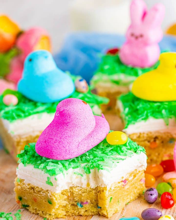 Side view of multiple Easter Sugar Cookie Bars topped with cream cheese, green coconut "grass", jelly beans, and brightly colored Easter Peeps.