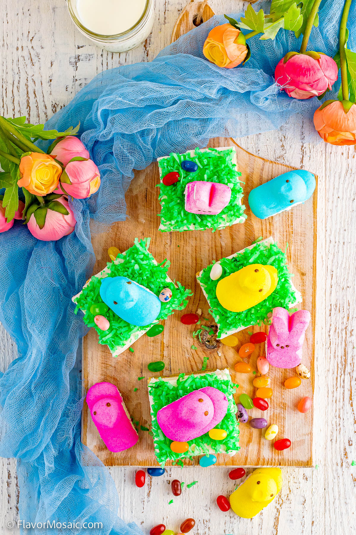 Overhead photo of Easter Sugar Cookie Bars on a board sitting on top of a white painted board surrounded by a blue mesh with pink flours on top.