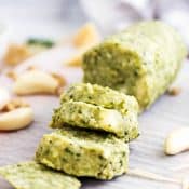 Pesto butter log cut into slices with garlic cloves and shredded parmesan cheese surrounding it.