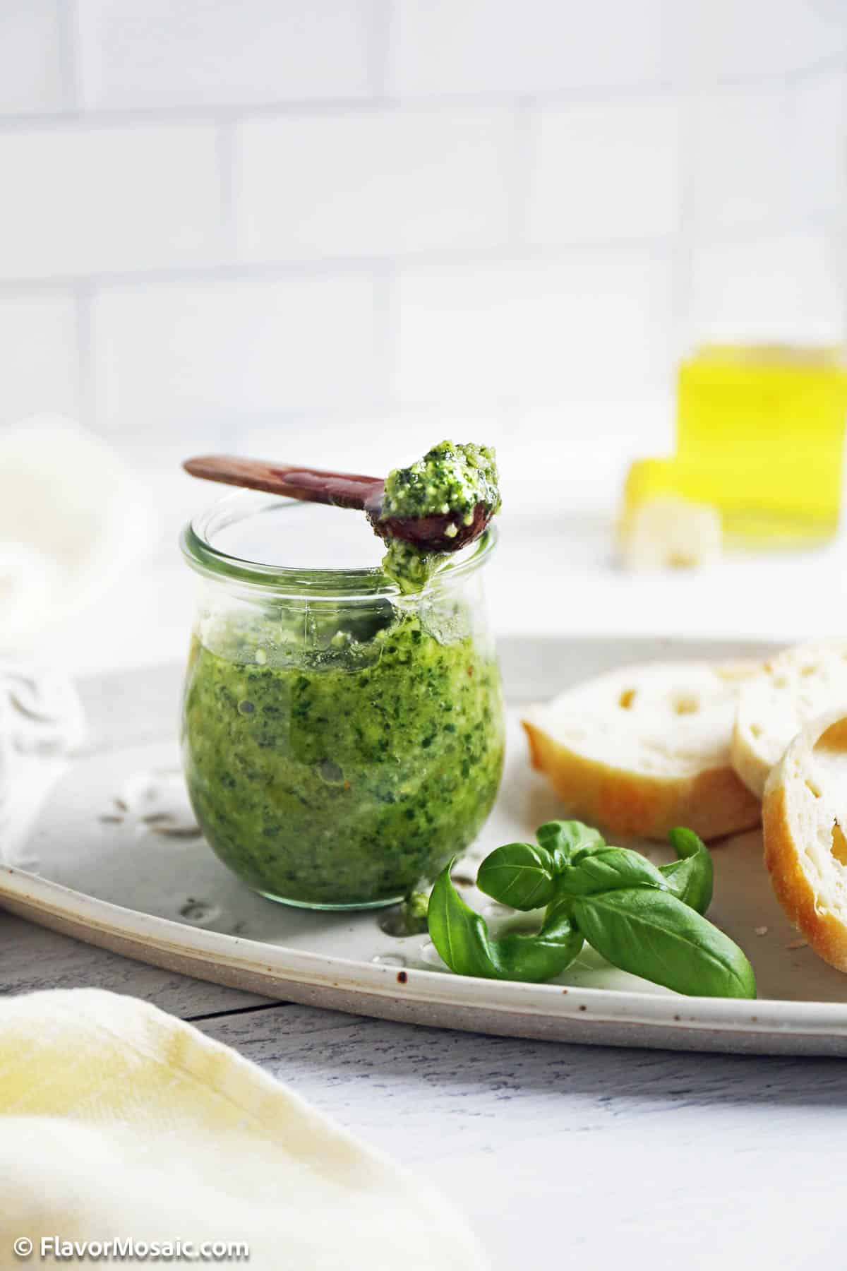 Side view of a jar of basil pesto with a wooden spoonful of pesto sitting on top of the pesto jar.