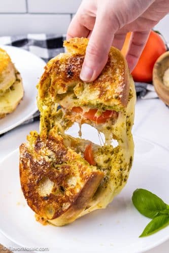 Two halves of Pesto Grilled Cheese sandwich being pulled apart with strings of melted mozzarella in between.