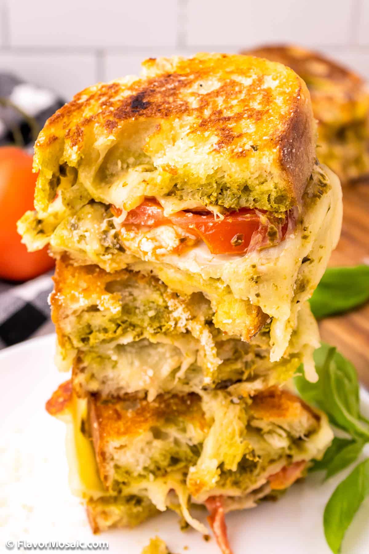 Pesto grilled cheese sandwich halves stacked on top of each other on a white plate.