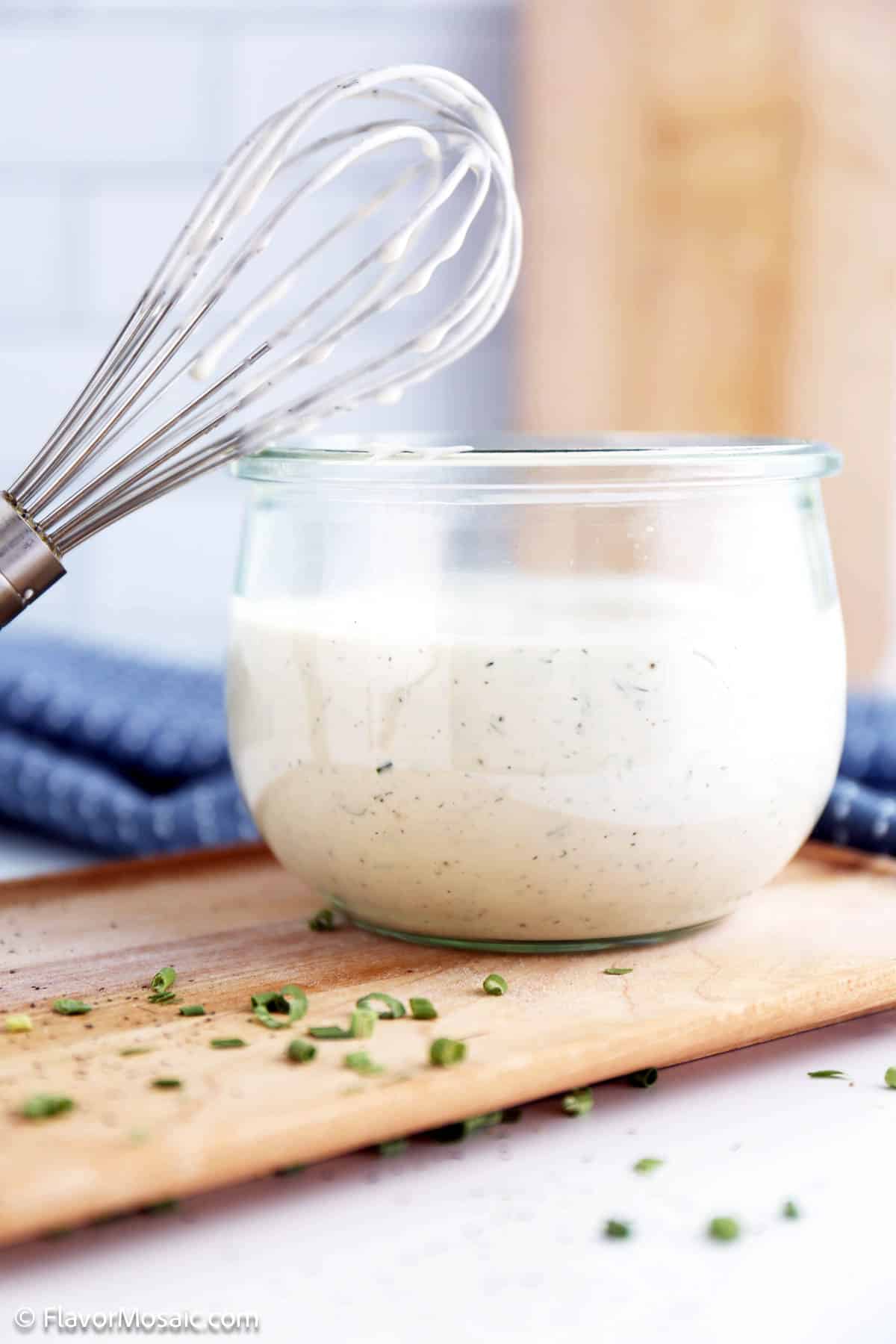 Side view small glass bowl of ranch dressing with a metal whisk leaning on it with ranch dressing on the whisk.