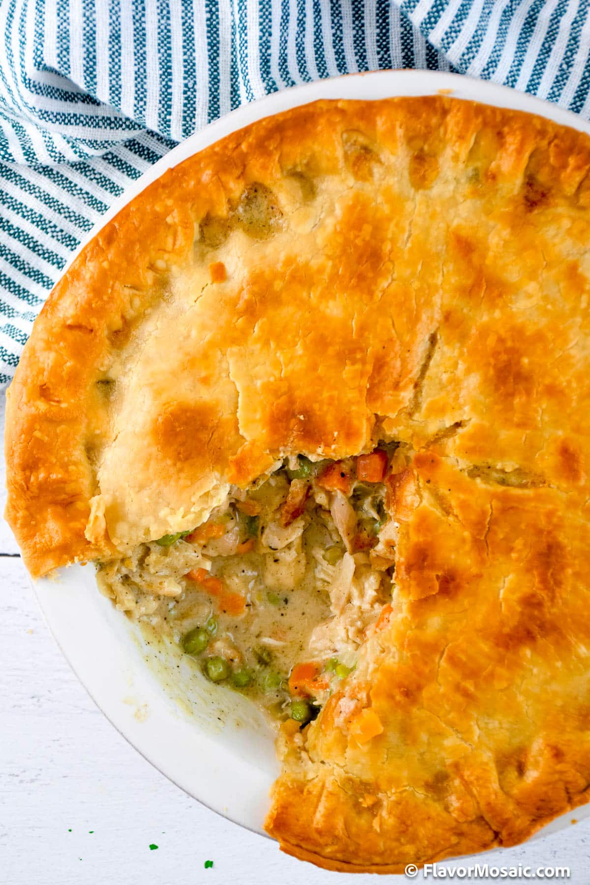 Overhead view of a whole chicken pot pie with one serving taken out of it so you can see the chicken and vegetables under the golden pie crust.