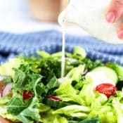 Side view pouring ranch dressing on a salad from a small glass pitcher.