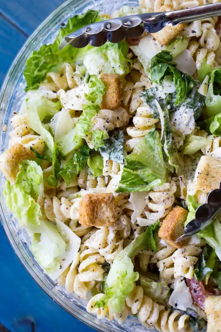 Rotini pasta with fresh crisp lettuce with Caesar Salad in a clear glass bowl.