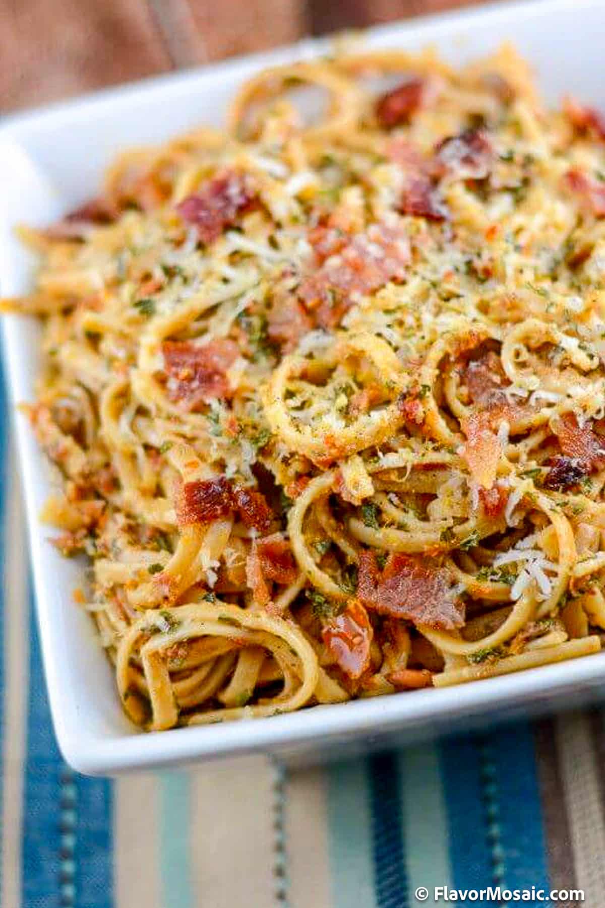 A white square bowl filled with Sun-Dried Tomato Pesto Pasta with bacon,  and parmesan cheese.