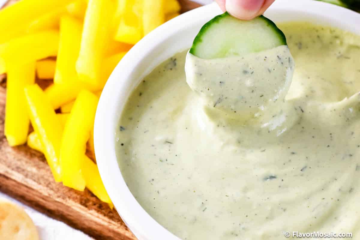 Dipping a cucumber into a white bowl of the avocado lime ranch dressing.