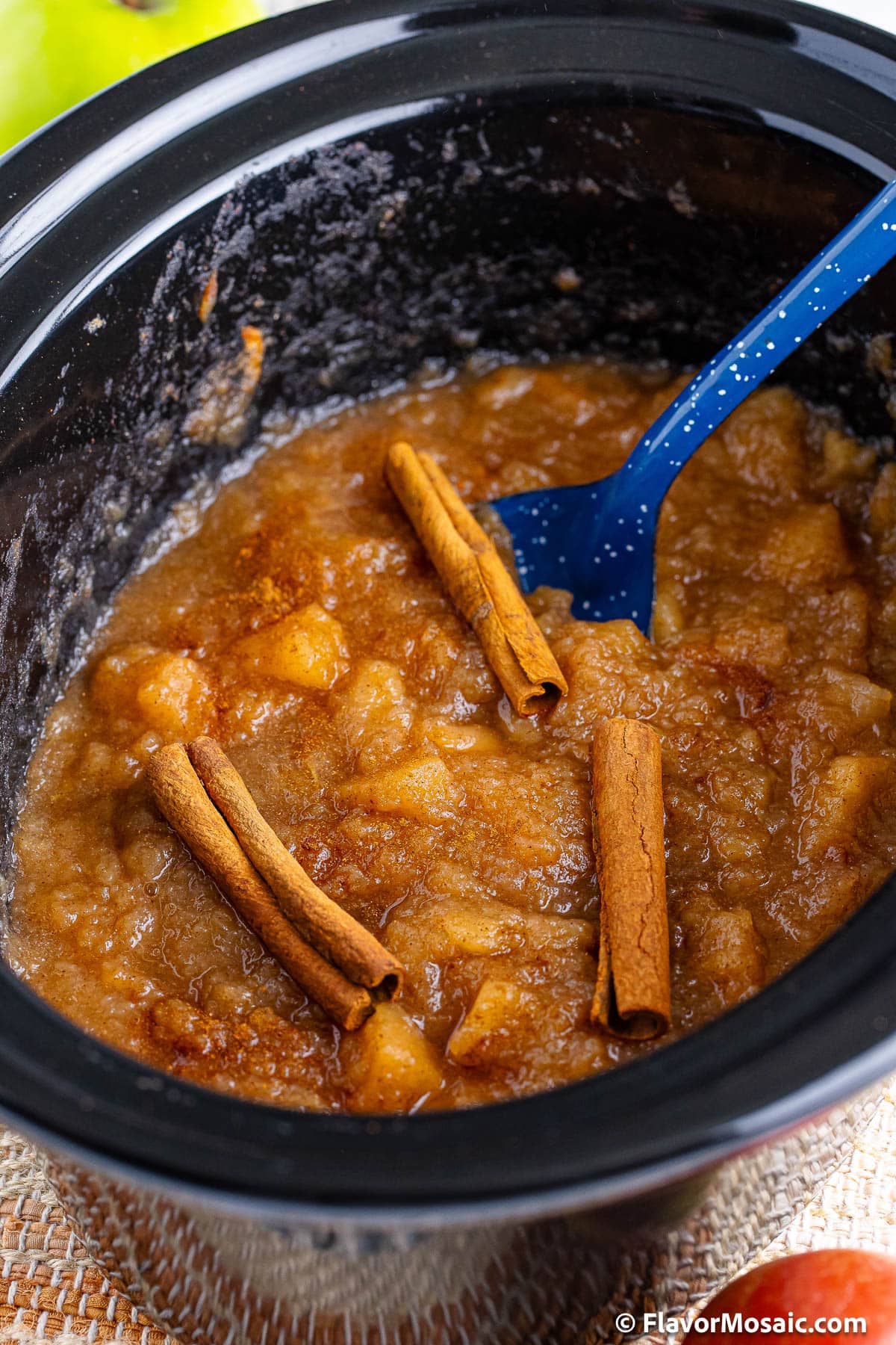 cooked applesauce in a slow cooker with cinnamon sticks on top.
