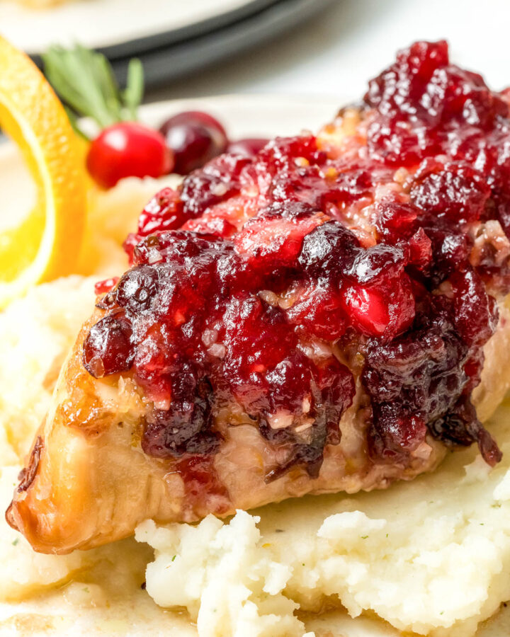 A single chicken breast covered with a flavorful cranberry sauce, sitting on top of mashed potatoes.