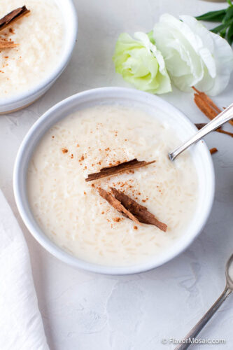 Overhead view of a white bowl of rice pudding with a cinnamon stick on top.