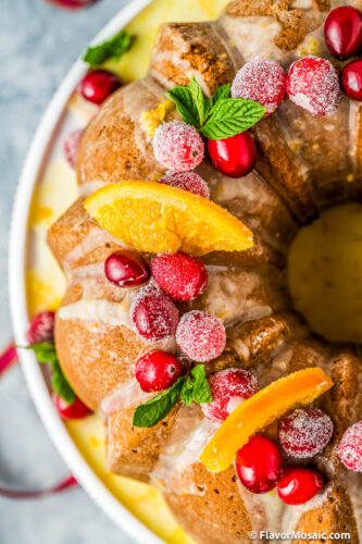 Overhead view of half of a Bundt Cake topped with candied orange slices, mint leaves, and sugared cranberries.