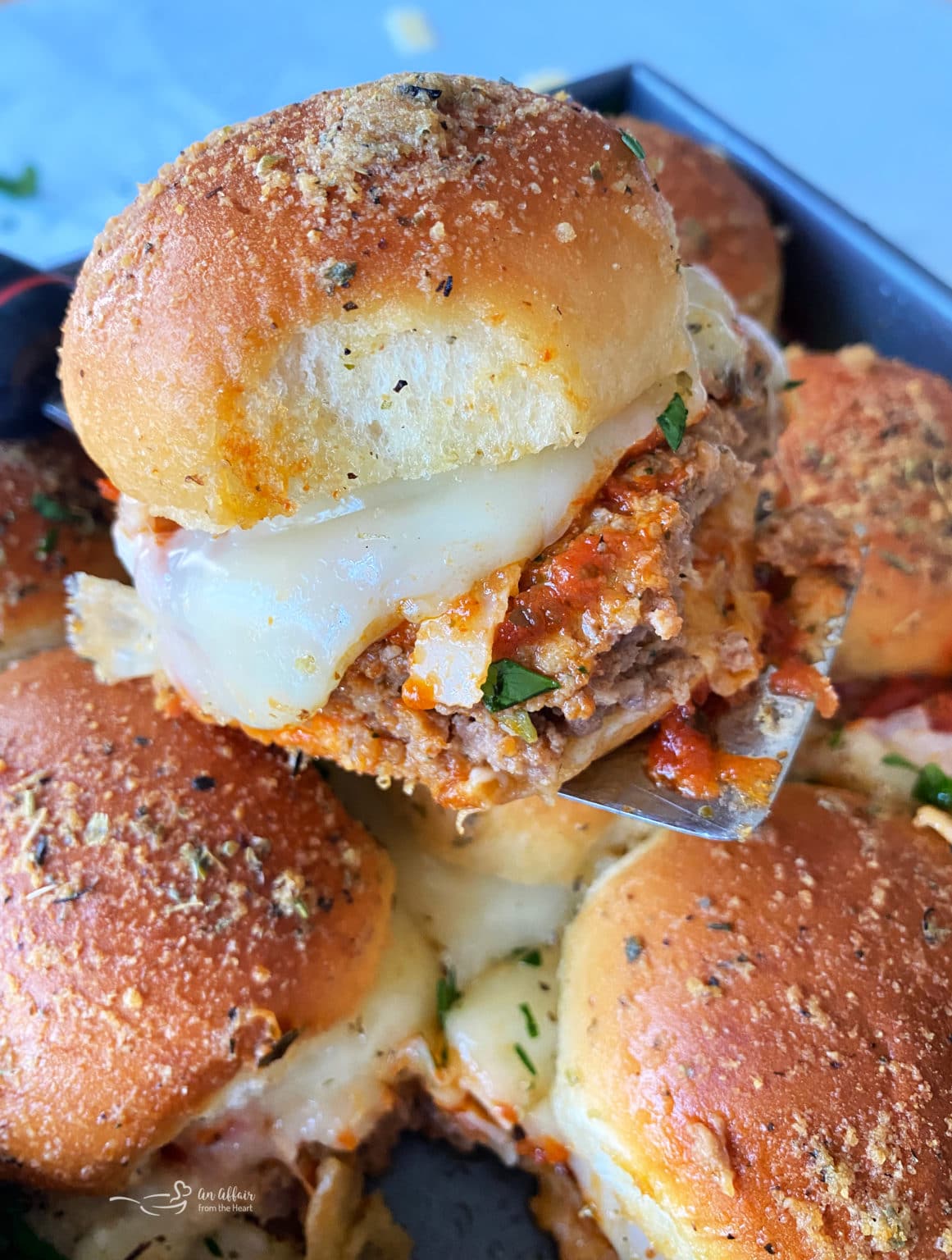 Italian Meatloaf Sliders with melted cheese on top of a spatula that is held above the rest of the sliders.
